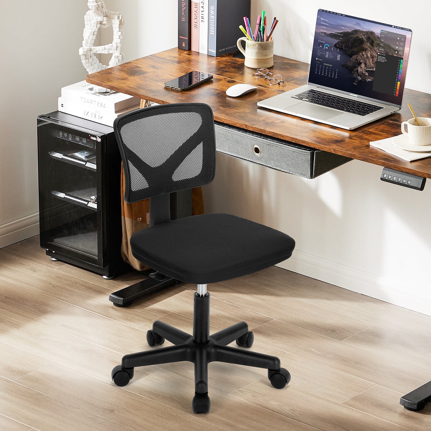 Black mesh office chair next to a wooden desk with a laptop and accessories