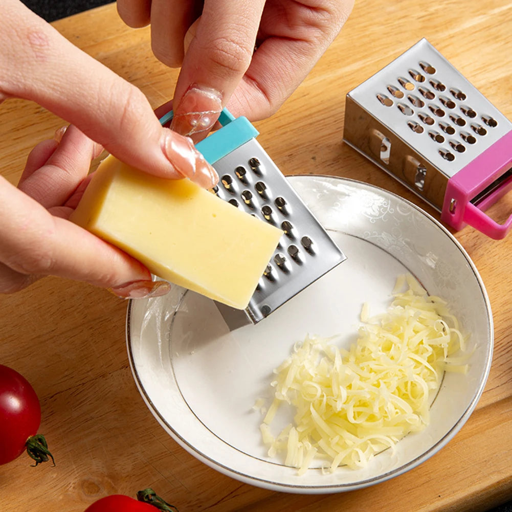Close-up of a hand using a mini stainless steel box grater with blue handle to grate cheese into a bowl