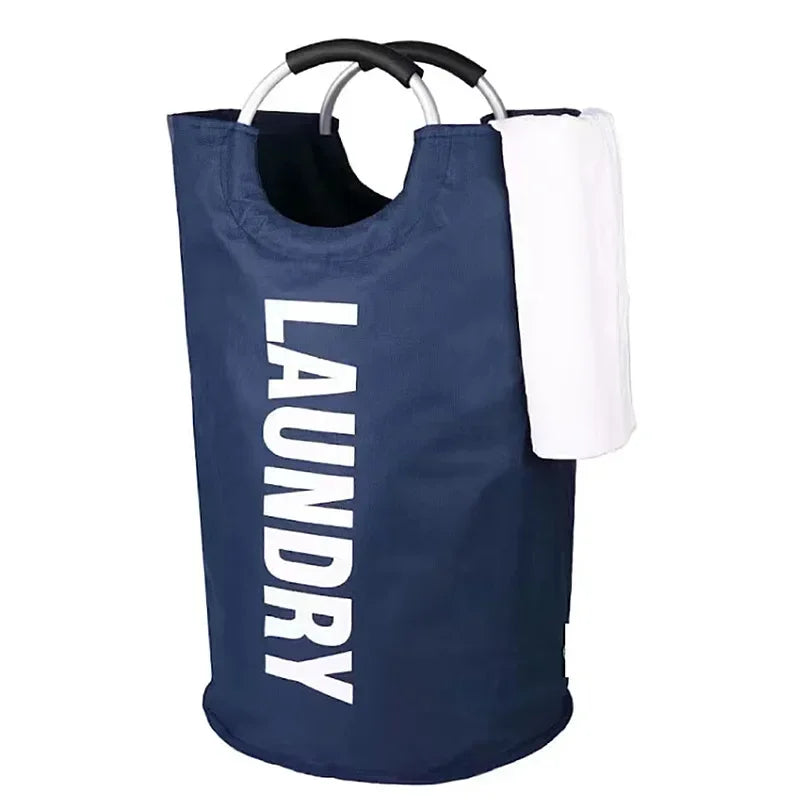 A navy blue cylindrical laundry hamper with aluminum ring handles and soft black grips, featuring the word "LAUNDRY" printed vertically in bold white letters. A folded white towel is draped over the side, and the hamper is standing upright on a white background.