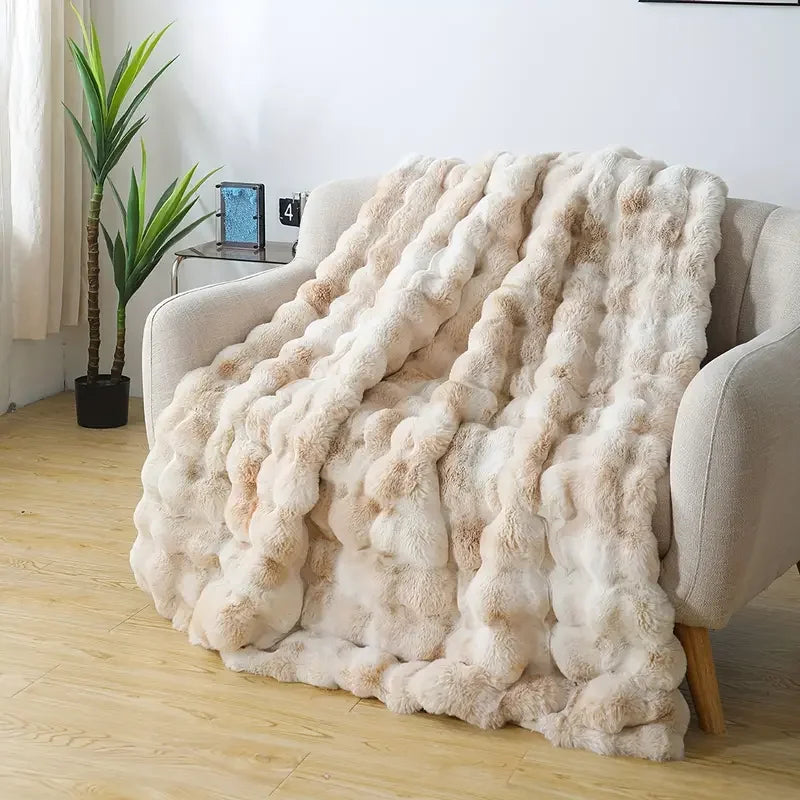 Beige faux-rabbit fleece blanket draped over an armchair in a bright living room, thick rippled pile.