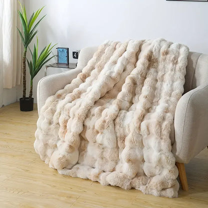 Beige faux-rabbit fleece blanket draped over an armchair in a bright living room, thick rippled pile.