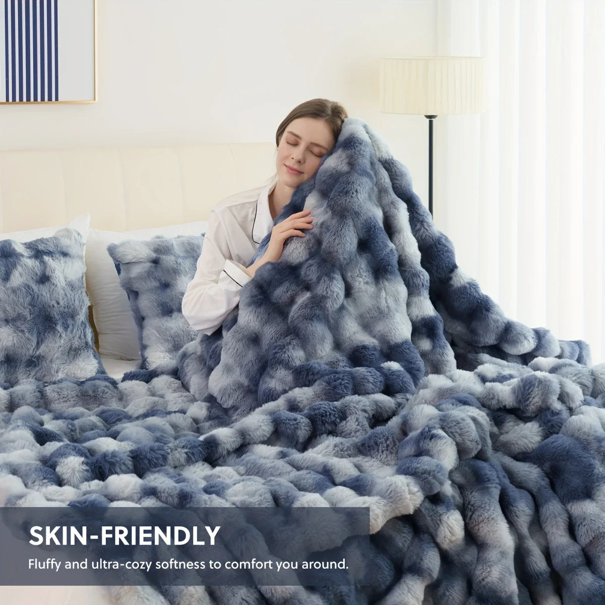 Woman cuddling a blue ombre dye faux-rabbit fleece blanket with matching pillows; “skin-friendly” callout on image.