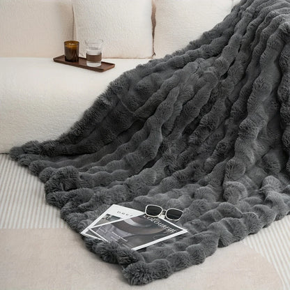 Dark gray faux-rabbit fleece throw cascading over a cream sofa with a wood tray, candle and glass.