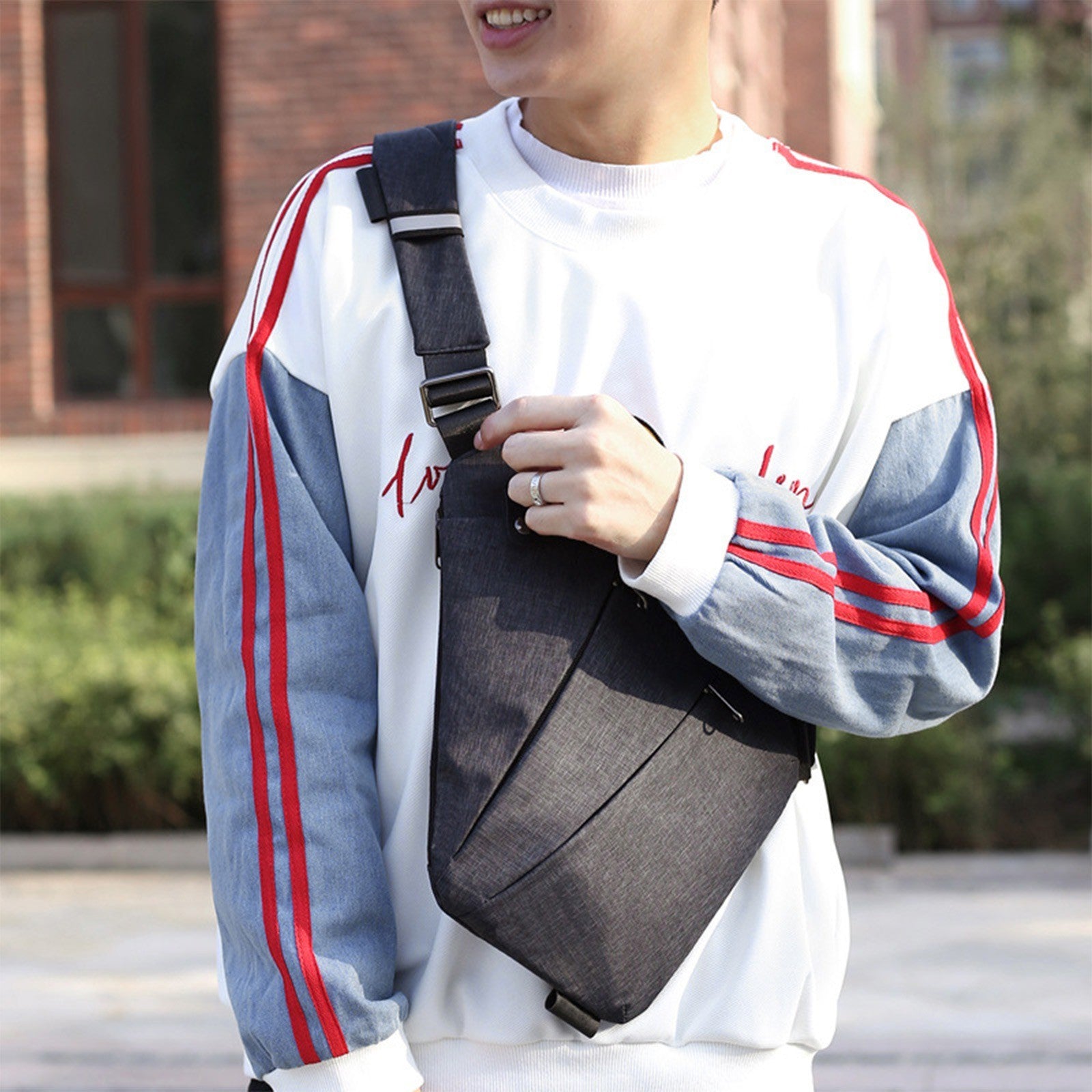 Man wearing dark grey sling chest bag over a sweatshirt in outdoor setting