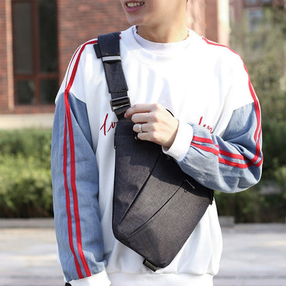 Man wearing dark grey sling chest bag over a sweatshirt in outdoor setting