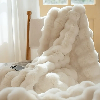 Ivory white faux-rabbit fleece blanket draped over a chair by a bright window, fluffy rippled texture.
