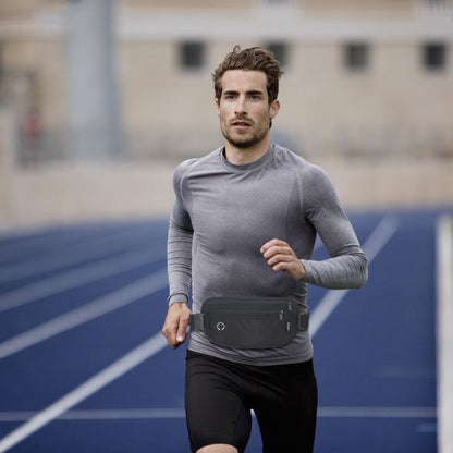 Athletic man jogging on a blue track while wearing a black waist pack around his waist, demonstrating its use during physical activities.
