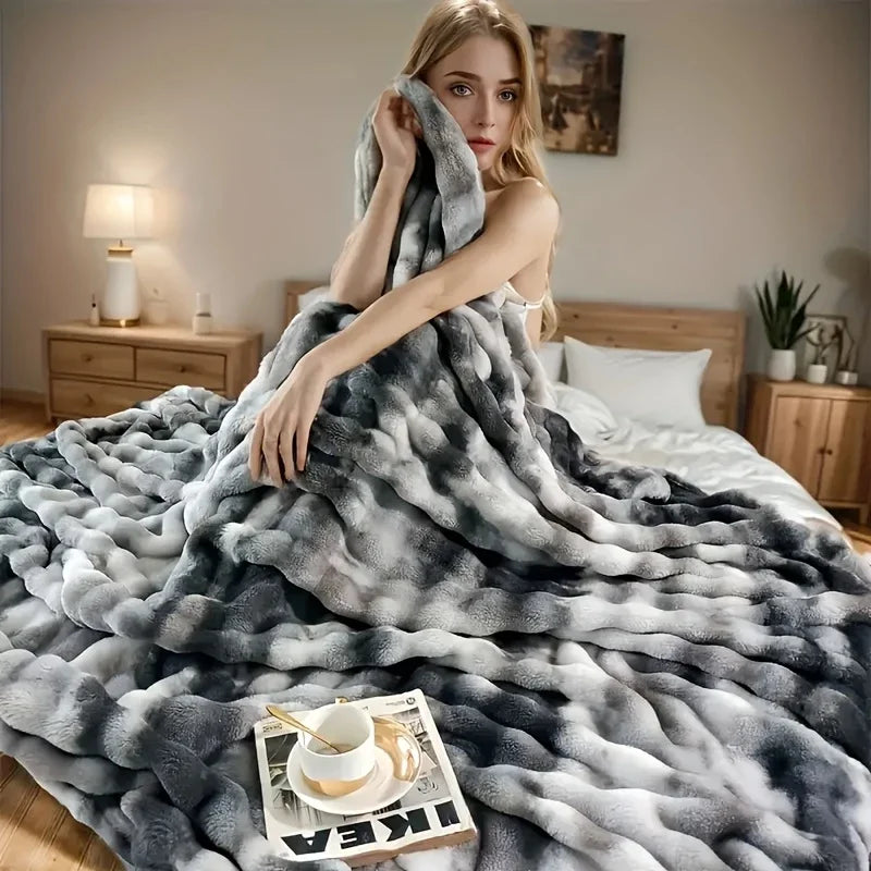 Model wrapped in an ombre gray dye faux-rabbit fleece blanket on a bed, cozy layered texture filling the room.