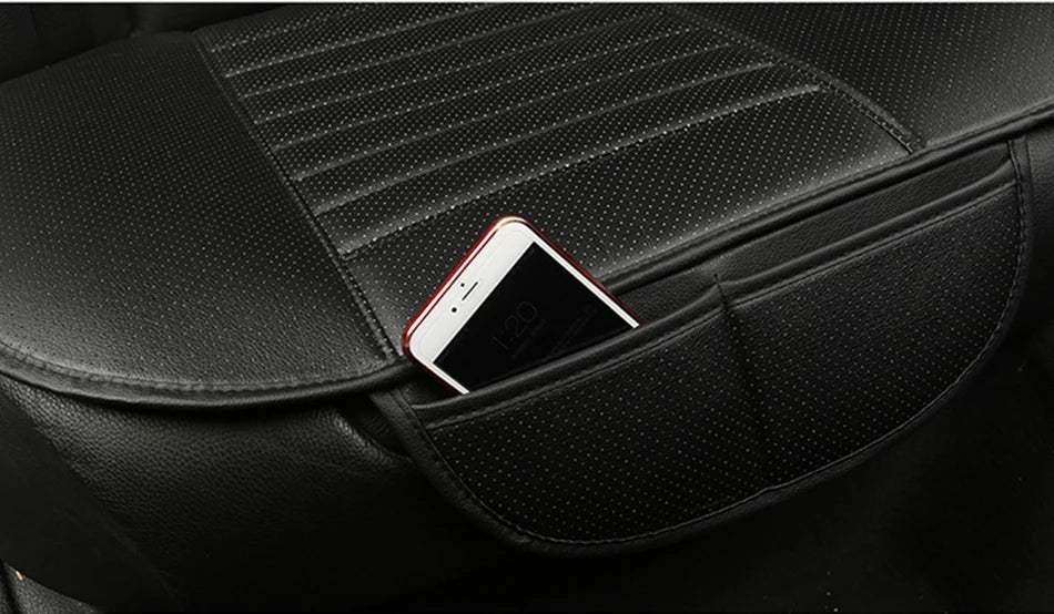 close-up of a black perforated leatherette car seat cushion with ribbed center panels, showing an integrated side storage pocket holding a smartphone