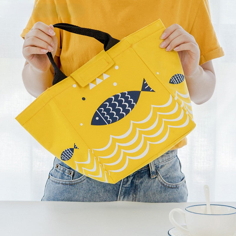 Person holding a yellow lunch bag with a blue fish and wave pattern.