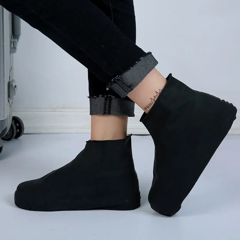 Black waterproof shoe covers on person seated beside luggage