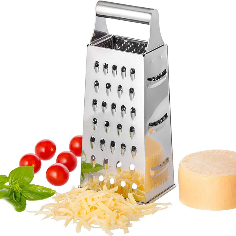  Stainless steel box grater standing upright next to grated cheese, cherry tomatoes, basil, and a cheese wheel on a white background