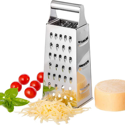 Stainless steel box grater standing upright next to grated cheese, cherry tomatoes, basil, and a cheese wheel on a white background