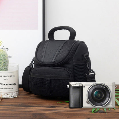 Black camera shoulder bag displayed on wooden surface beside a mirrorless camera, featuring front mesh pocket and padded top handle.