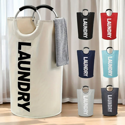 A cream-colored cylindrical laundry basket with a gray towel draped over one handle, placed in a softly lit indoor setting. The image also displays six additional color options—black, red, navy blue, light blue, light gray, and dark gray—on the right side.
