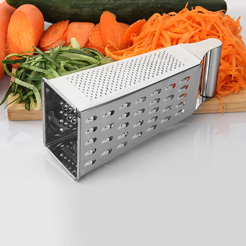 Stainless steel grater positioned horizontally next to freshly sliced cucumbers, carrots, and other vegetables on a cutting board