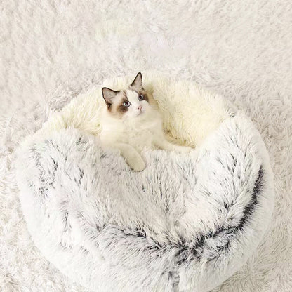  White and gray long-haired cat sitting in a round, plush donut-style pet bed with faux fur fabric, placed on a matching white rug.