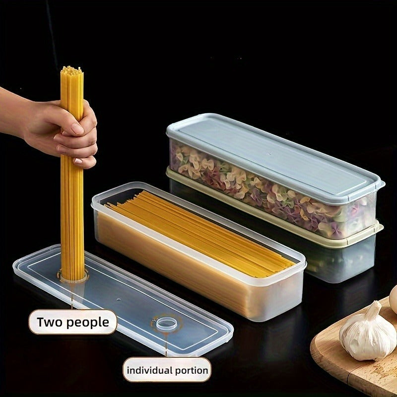 Three rectangular containers shown against a black background: one filled with colorful pasta, another with uncooked spaghetti. A hand is using the lid’s built-in portion guide to measure spaghetti for one or two servings. Garlic bulbs and a cutting board are visible nearby.