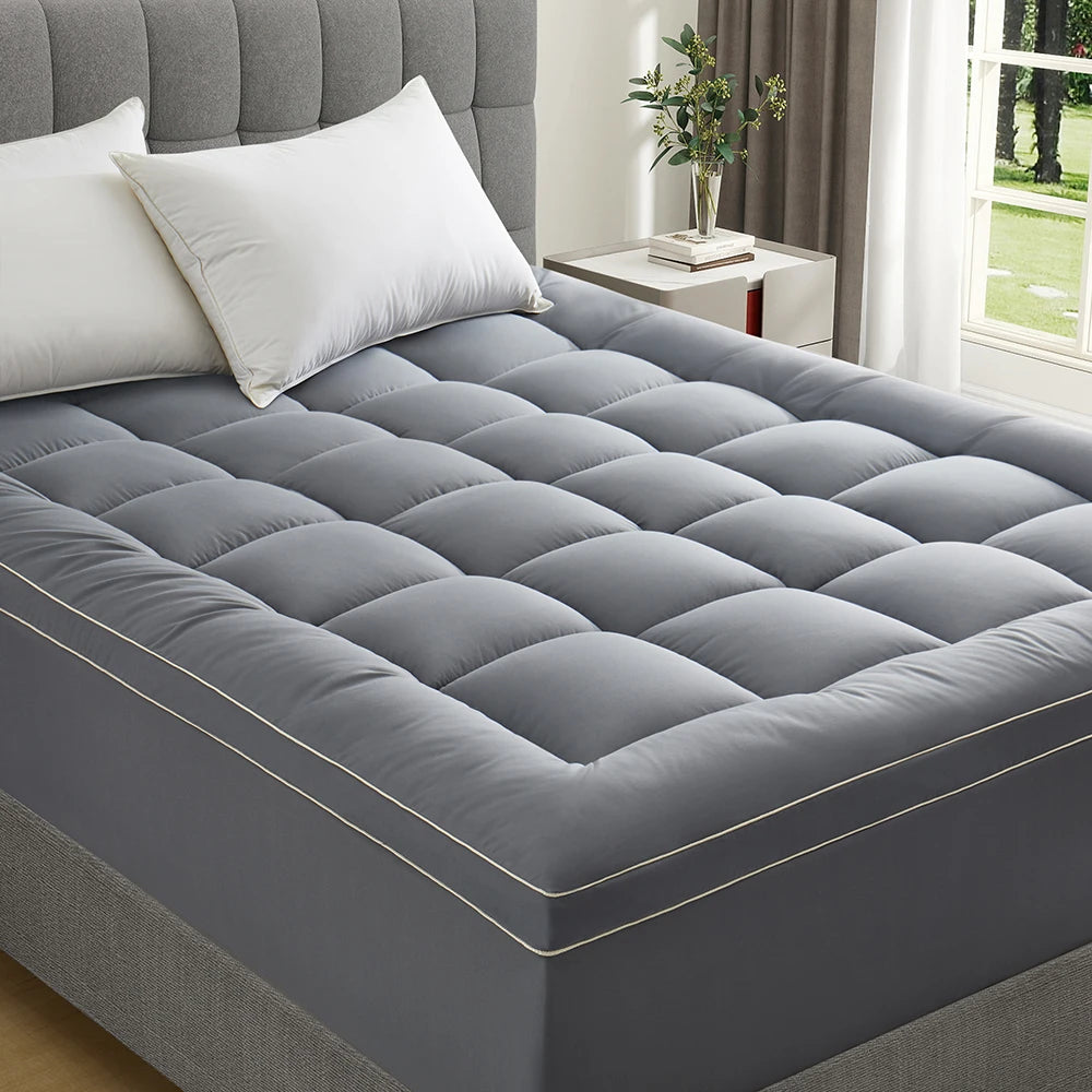 Quilted gray mattress topper fitted on bed in bright bedroom