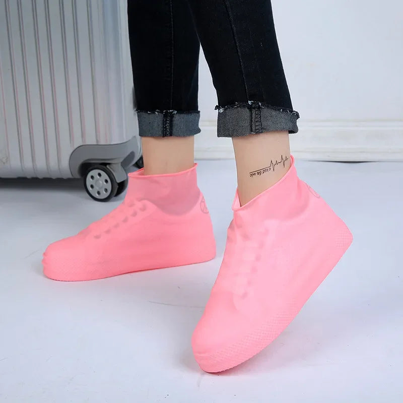Pink waterproof silicone shoe covers on feet beside a suitcase