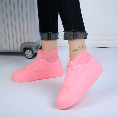 Pink waterproof silicone shoe covers on feet beside a suitcase