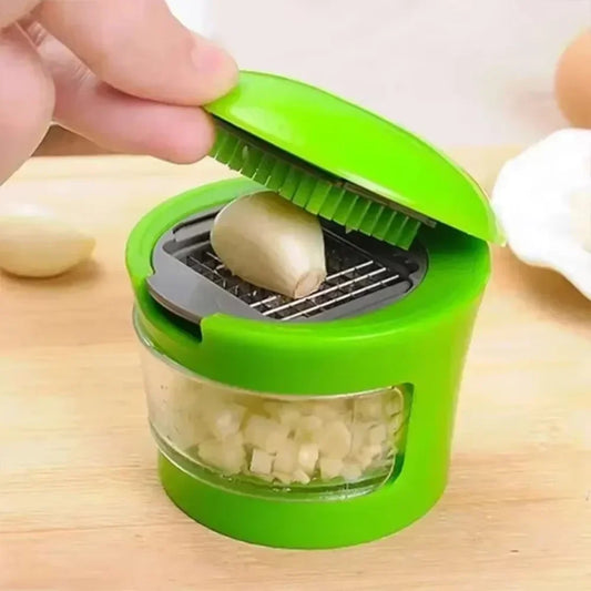 Hand pressing garlic clove into green manual garlic chopper with clear container collecting diced pieces