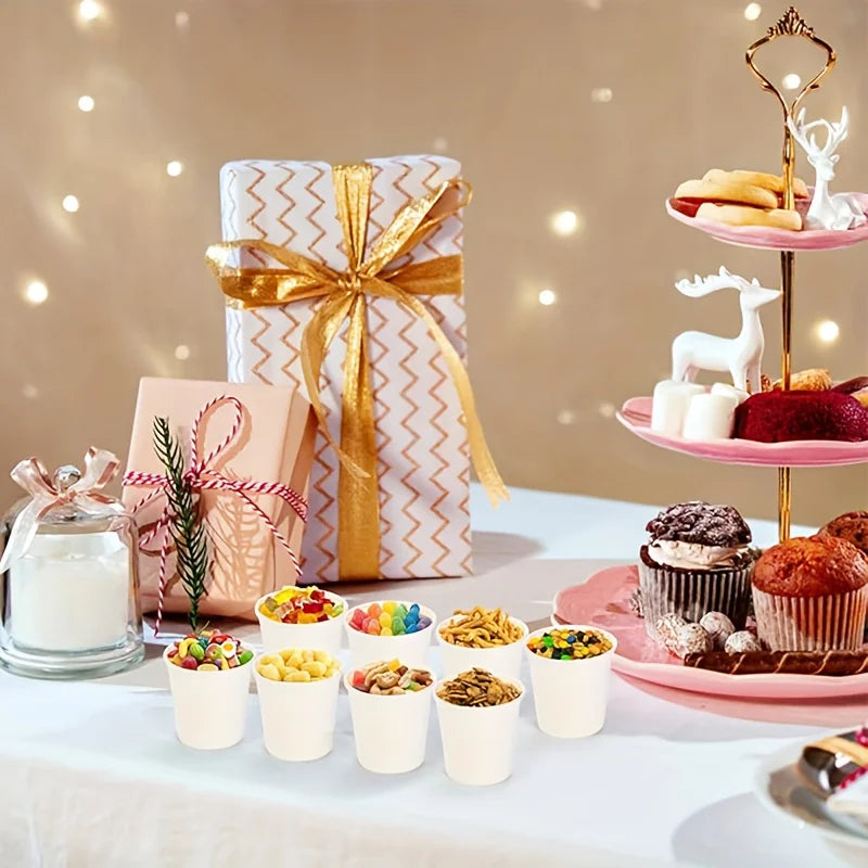 Disposable paper cups filled with snacks on a party dessert table with gifts and cupcakes.